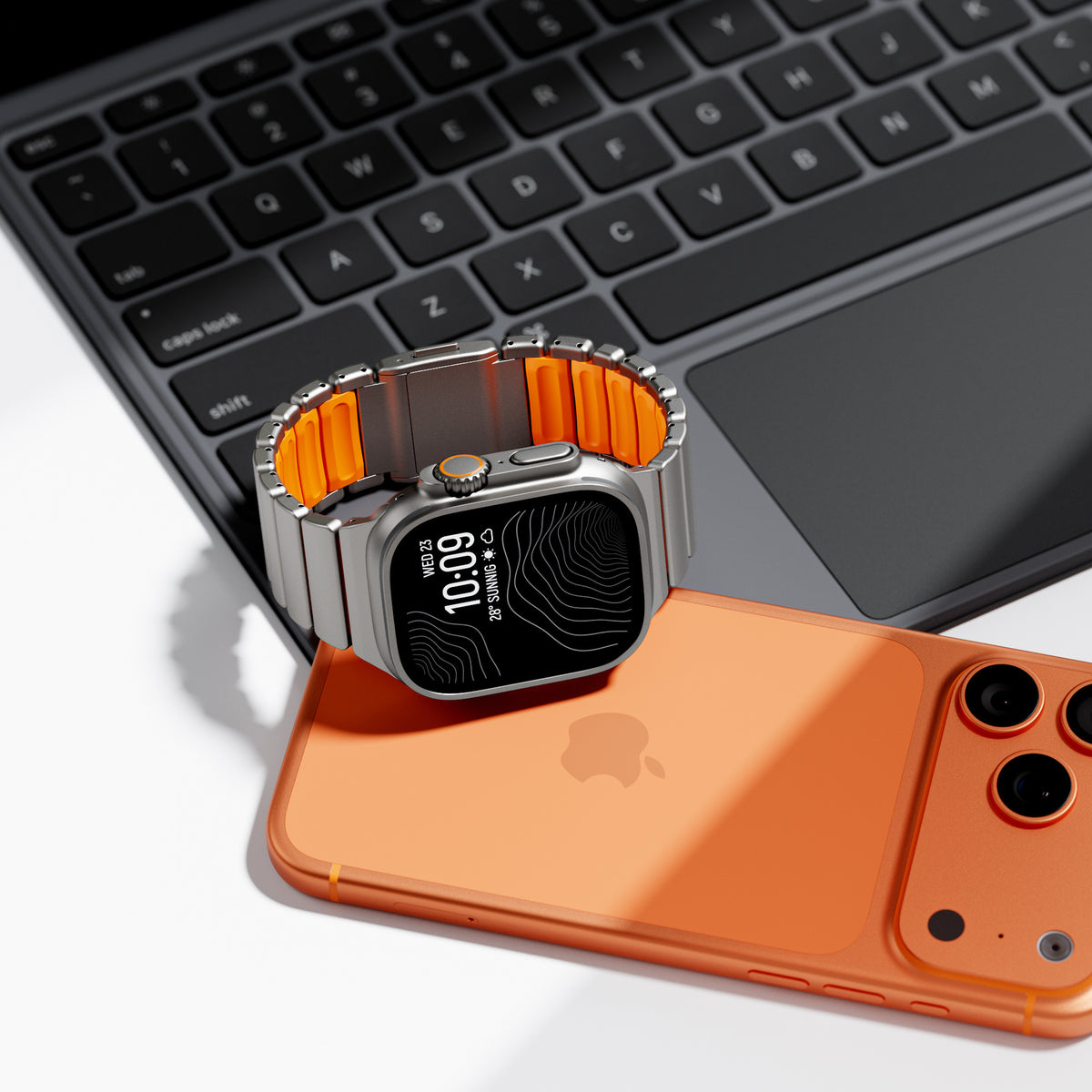 Titanium and orange silicone Apple Watch band by a laptop
